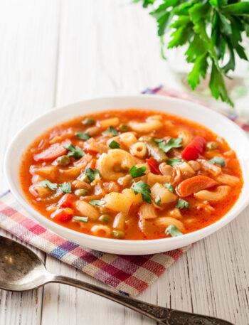 Bowl of Minestrone on a checkered napkin with a spoon next to it.