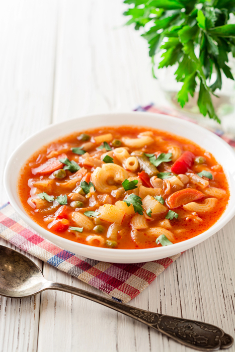 Bowl of Minestrone on a checkered napkin with a spoon next to it.