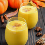 Pumpkin Spice Smoothies on a wood surface with pumpkins and cinnamon sticks.