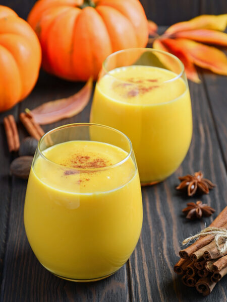 Pumpkin Spice Smoothies on a wood surface with pumpkins and cinnamon sticks.