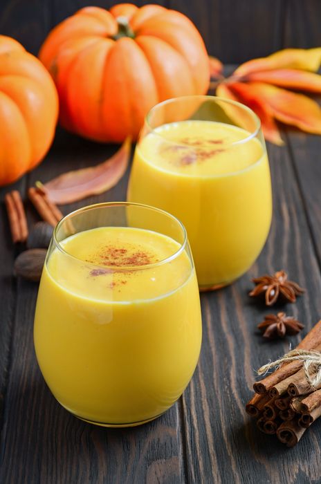 Pumpkin Spice Smoothies on a wood surface with pumpkins and cinnamon sticks.