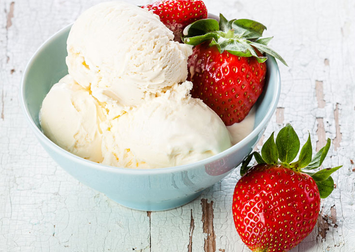 Bowl of vanilla ice cream with whole strawberries.