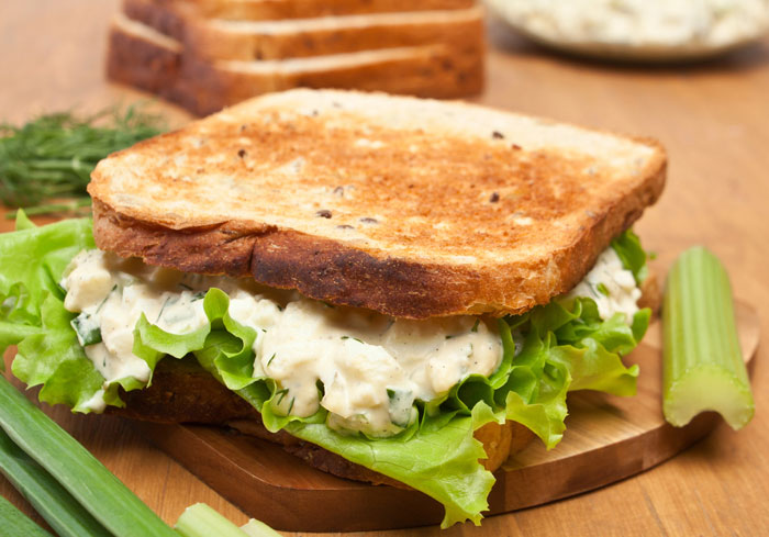 Toasted vegan egg salad sandwich on a cutting board with a piece of celery beside it.