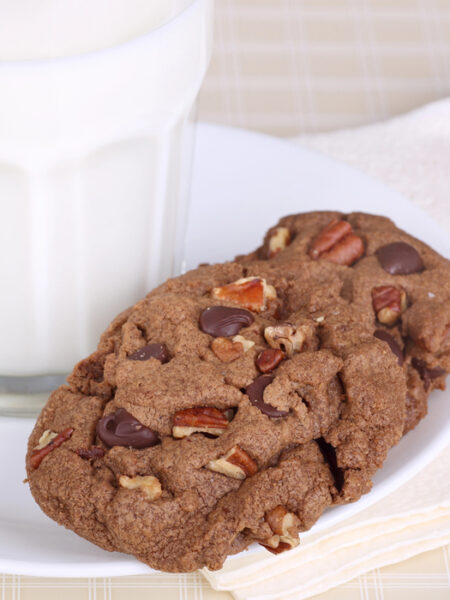 Two vegan double chocolate walnut cookies on a white plate with milk.