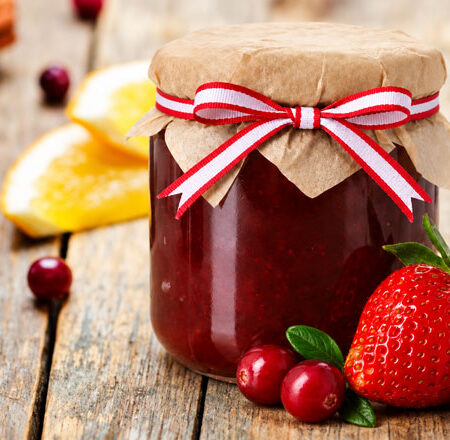 Jar of Cranberry Strawberry Holiday Jam with a red and white bow, and strawberries, cranberries, and oranges slices.
