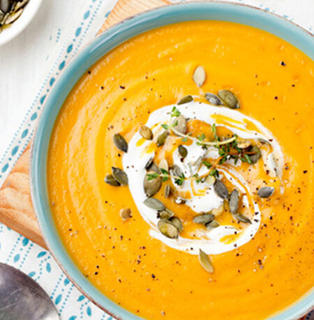 Bowl of Creamy Vegan Pumpkin Soup with a swirl of dairy-free cream and toasted pumpkin seed garnish.
