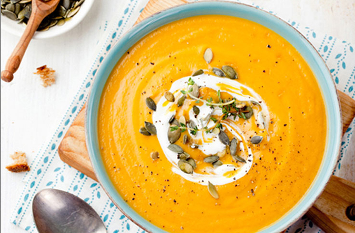 Bowl of Creamy Vegan Pumpkin Soup with a swirl of dairy-free cream and toasted pumpkin seed garnish.