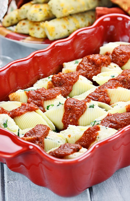 Red baking dish with vegan stuffed shells with marinara.
