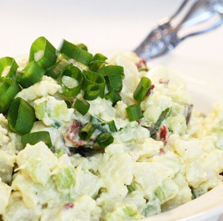 Bowl of Vegan Potato Salad topped with green onion and a serving spoon.