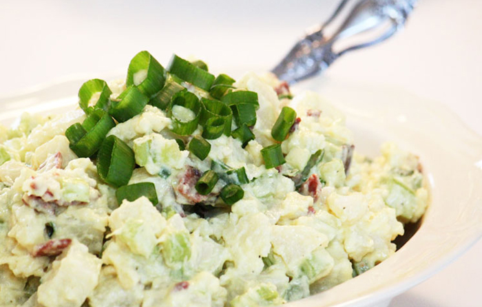 Bowl of Vegan Potato Salad topped with green onion and a serving spoon.